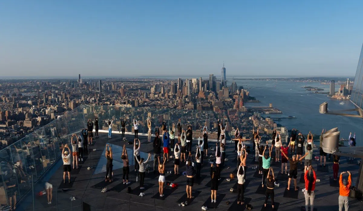Group practicing yoga on outdoor sky deck with NYC skyline in background.
