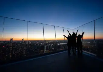 Three people raise their arms in celebration at The Edge at sunset