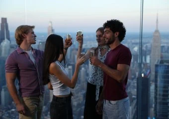 Group of friends enjoying drinks with NYC skyline view from Edge NYC sky deck.
