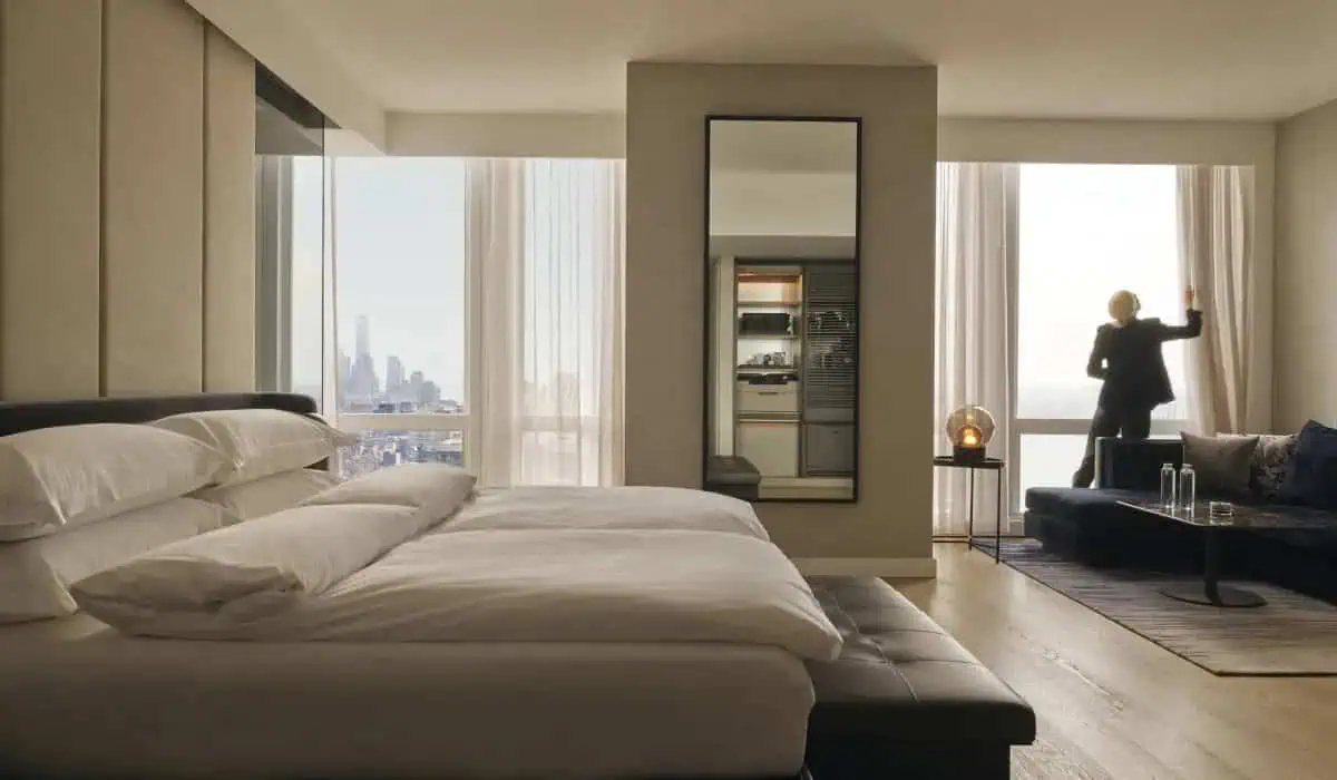 A king suite at Equinox, a woman pulling back curtains to let light in