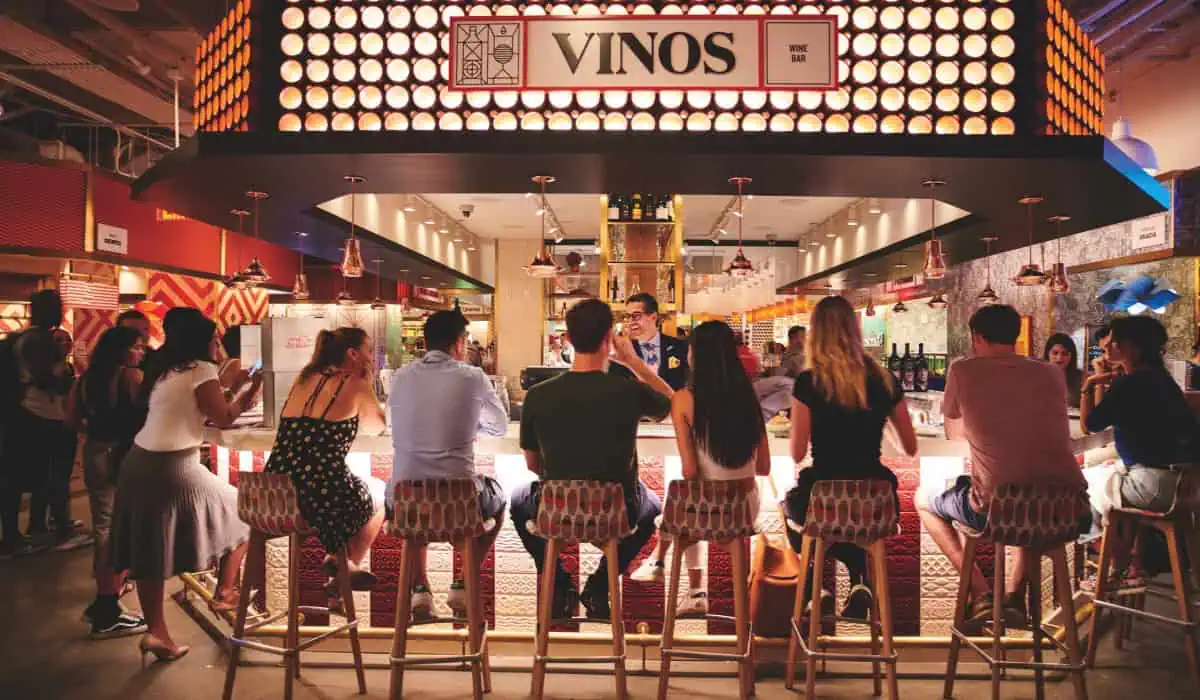 A group of people laugh and drink at the bar at Mercado Vinos