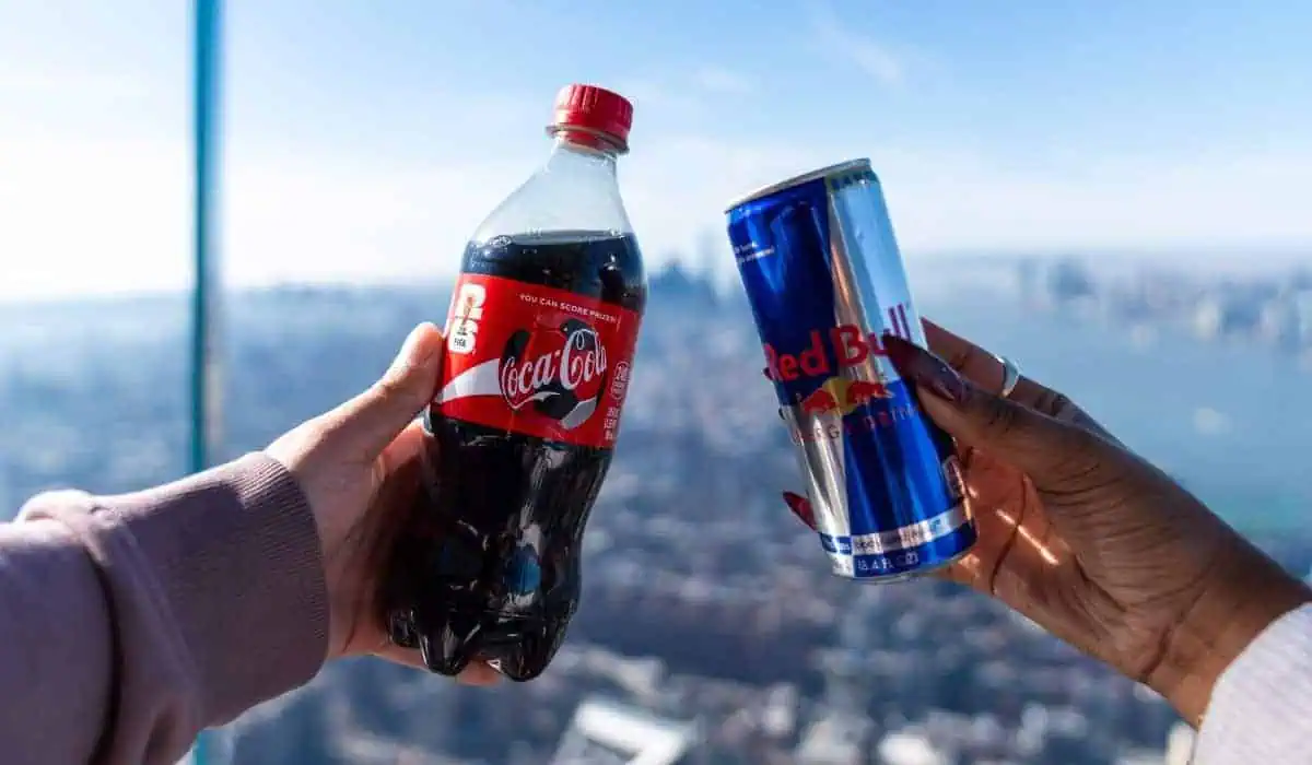 two hands holding a coca cola and redbull with the nyc skyline in the background