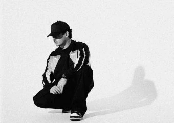 Person crouching in black and white with cap and sneakers on plain background.