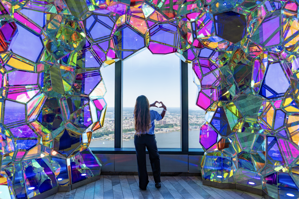 Woman inside colorful, illuminated Crystal Cave installation at Edge NYC taking photos.