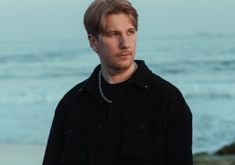 Young man with blond hair and tattoos looking at the ocean on a cloudy day.