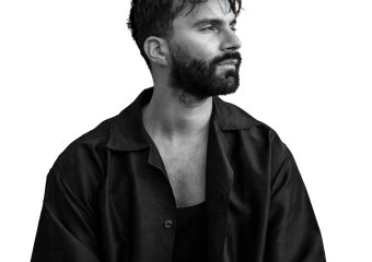 Black and white portrait of a man with a beard and curly hair, looking to the side.