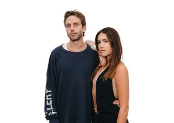 Man in a navy sweater stands beside a woman in black, posing together against a white studio background.