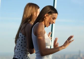 Two women looking out a window at NYC skyline from Edge NYC sky deck.