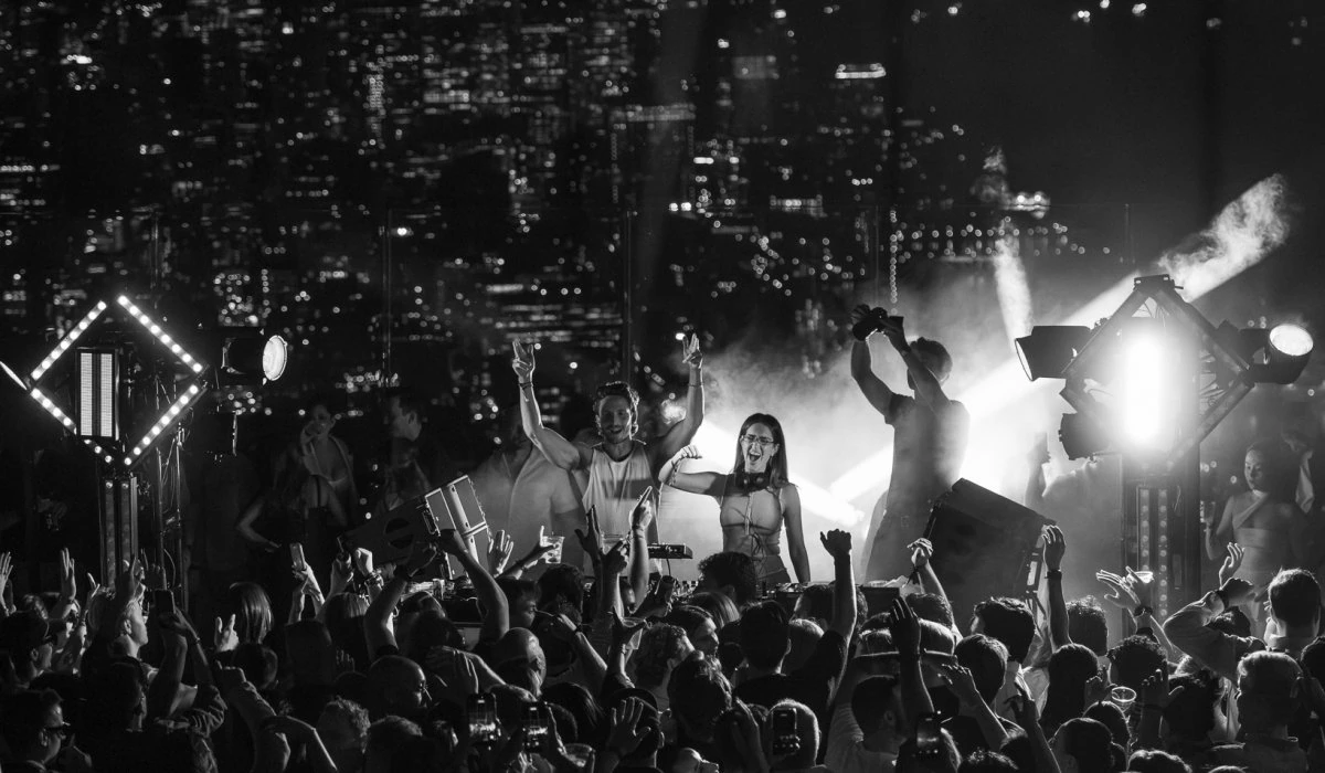 Nighttime crowd at Edge NYC with city skyline in background.