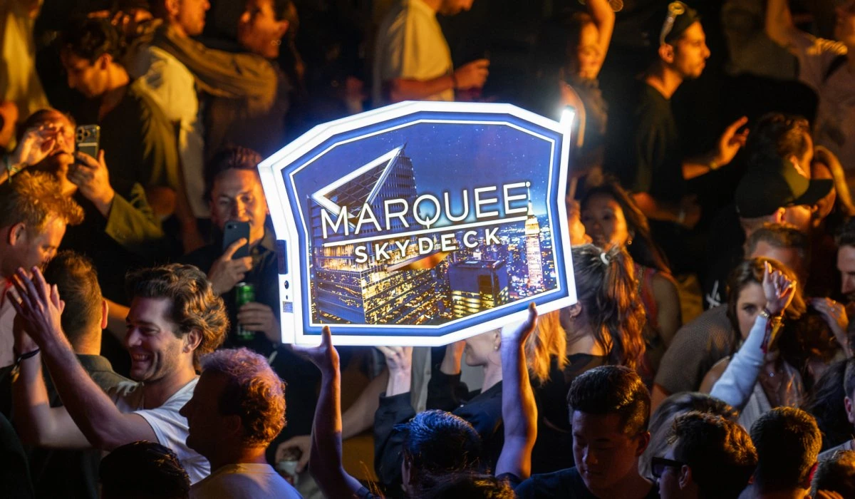 Crowd at Edge NYC outdoor sky deck with illuminated marquee sign at night.