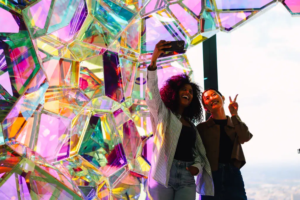 Two-girls-taking-pictures-at-Crystal-Cave-Immersive-experience-at-edge - Edge NYC - Edge NYC Two women taking a selfie at Edge NYC with Crystal Cave behind them.