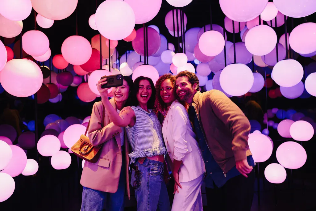 people-taking-pictures-at-pulse-immersive-experience-at-edge - Edge NYC - Edge NYC Group of friends taking a selfie under colorful hanging lights at Edge NYC.