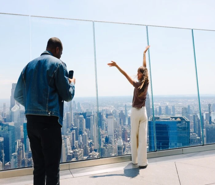 Two people on the Edge NYC sky deck with Manhattan skyline in background.