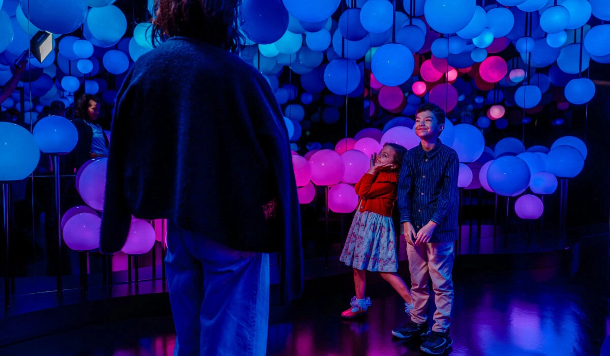 A doorway of blue and pink balloon installation with two children smiling, viewed from behind an adult in the foreground.