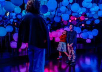 A doorway of blue and pink balloon installation with two children smiling, viewed from behind an adult in the foreground.