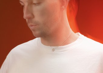 Portrait of a man with short dark hair in a white T-shirt, looking down to the left with a warm red backlight.