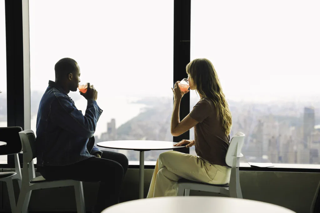 Couple enjoying drinks at Edge NYC - Edge NYC - Edge NYC Couple drinking cocktails while sitting by a large window at Edge NYC with city views.