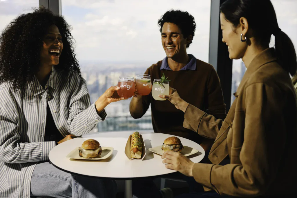People enjoying food and drinks at Edge NYC with city skyline view.
