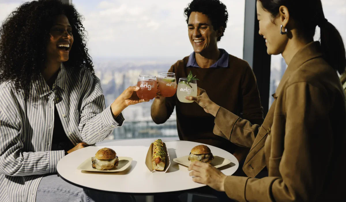People enjoying food and drinks at Edge NYC with city skyline view.