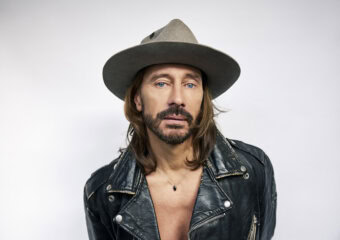 Man with long hair, beard, leather jacket, and wide-brimmed hat.